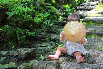 Little baby wearing a traditional yukata custom plays with forest leaves while sitting over the...
