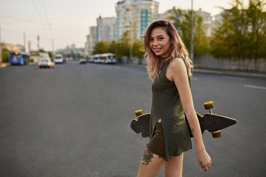 Beautiful girl with tattoos posing with a colorful longboard