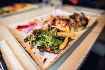 Close up focus view of fried chips and salad with fried skewers on a wooden stick behind in the plate in the restaurant.