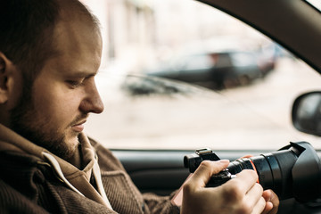 Investigator or private detective or reporter or paparazzi sitting in car and taking photo with...