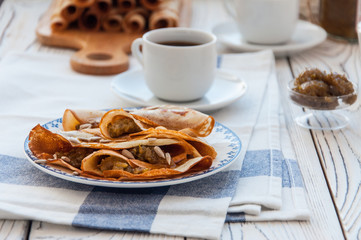 Thin pancakes for breakfast. Maslenitsa. On the table, a dish with pancakes, coffee and jam from feijoa