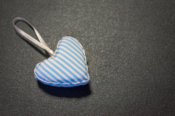 Fototapeta na wymiar Top view of a blue and white striped textile, fabric heart isolated on dark gray background. Love, romance or Happy Valentine's Day concept