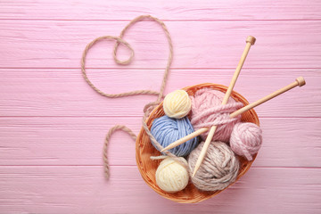 Balls of knitting yarn in basket and heart made of thread on wooden background