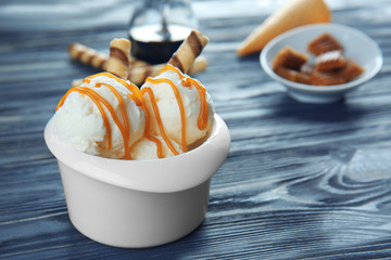 Bowl with ice cream and caramel sauce on wooden table