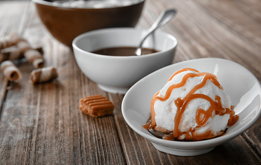 Bowl with ice cream and caramel sauce on wooden table