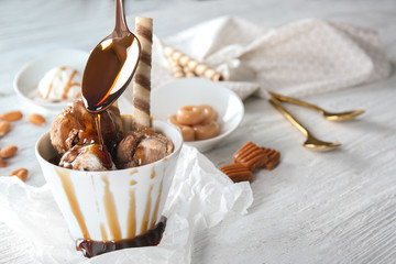 Fototapeta na wymiar Pouring caramel sauce into bowl with ice cream on table