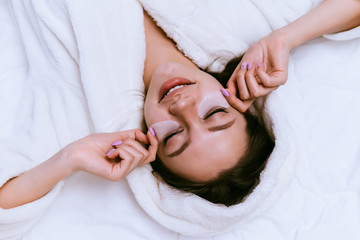 a woman put patches under her eyes and lies on the bed