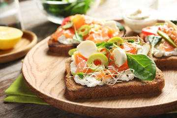 Tasty bruschettas with olives and salmon on wooden plate