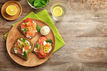 Tasty bruschettas with olives and salmon on wooden plate