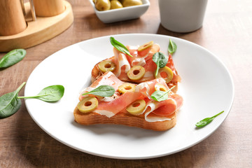 Tasty bruschettas with olives and prosciutto on plate