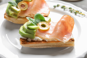 Tasty bruschettas with avocado and prosciutto on plate, closeup