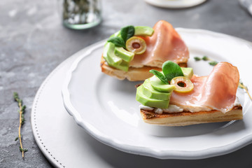 Tasty bruschettas with avocado and prosciutto on plate