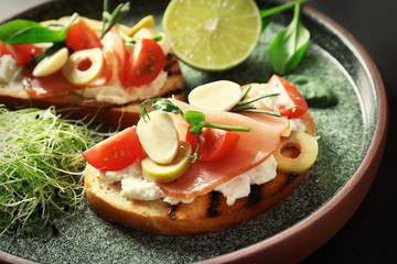 Tasty bruschettas with prosciutto, tomatoes and mozzarella on plate, closeup