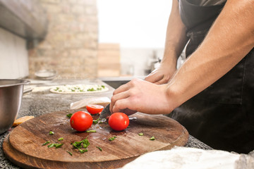 Chef preparing topping for pizza at table in restaurant kitchen