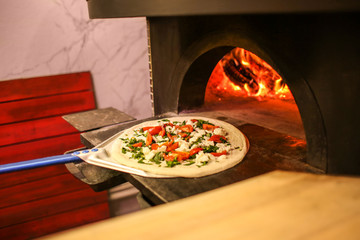 Putting traditional pizza into oven at restaurant kitchen