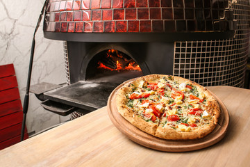 Tasty pizza on table against stove in kitchen