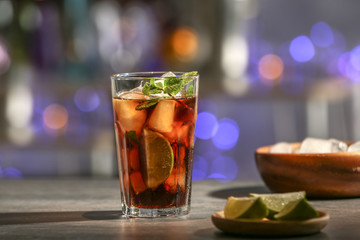 Glass with Cuba Libre cocktail on table against blurred background