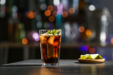 Glass with Cuba Libre cocktail on table against blurred background