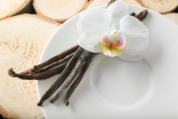 Plate with vanilla sticks and flower on wooden stumps