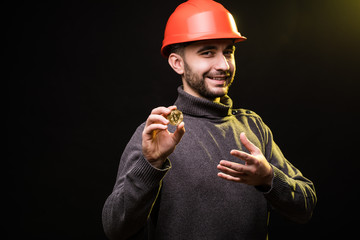 Handsome man miner in protective hemlet present bitcoin isolated on black background