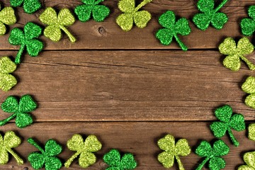 St Patricks Day frame of glittery shamrocks over an old rustic wood background