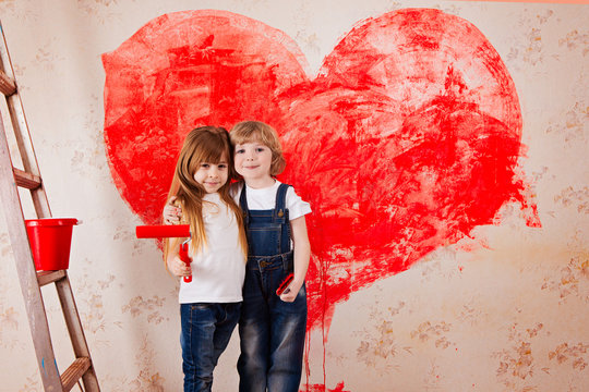 a boy and a girl with a roller in jeans and a white T-shirt, a brush and a bucket paint the wall in red.