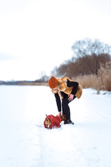 beautiful girl in a fur vest plays with a dog in the snow