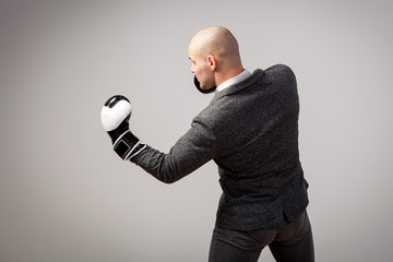 Bald man, confident manager in a white shirt, gray suit and boxing gloves makes an uppercut on a white isolated background, side view - obrazy, fototapety, plakaty