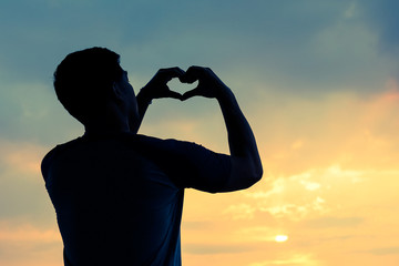 The silhouette of man hand holding a heart symbol on a sunset