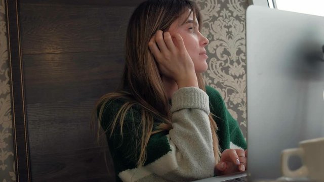 Beautiful girl model sitting at a table in a cafe and working on the computer