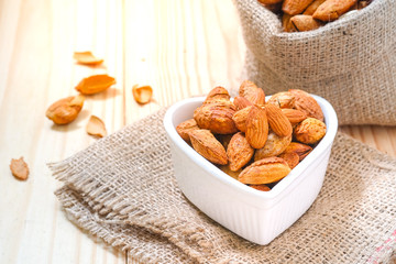 Almond nuts in the shell In a heart shaped bowl on sackcloth and wooden floor.
