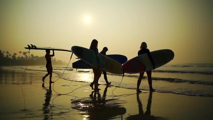 Silhouette surfers with surfboard come into the water sunrise rapid slow motion 