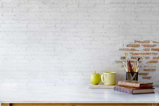 Front view of Artist or Designer desk with creative tools, vintage books and coffee mug over white brick wall. copy space for product display montage.