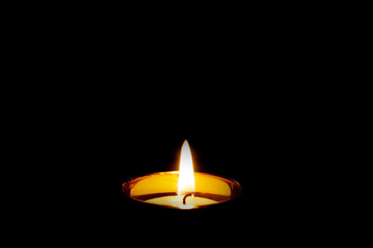 Mourning funeral concept. Single isolated burning yellow candle flame on black. Pet or human condolences.