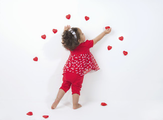 Mixed race, little, girl decorates white wall with red hearts for Valentine's Day