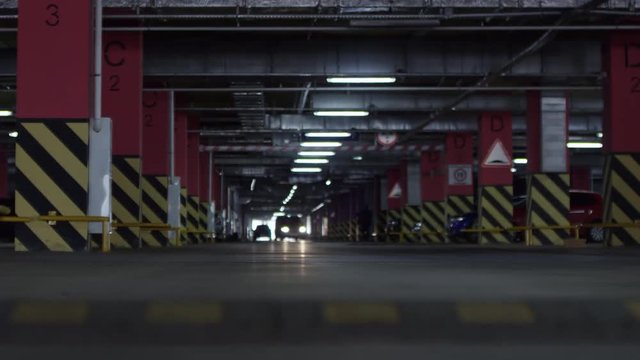 Low angle shot with rack focus of vehicle driving through dark underground parking lot with speed bump