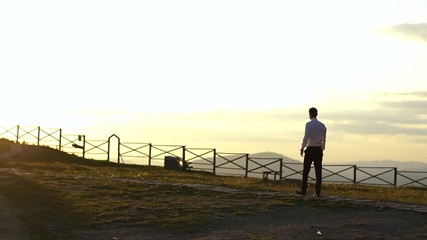 Isolated man is walking along the path at the background of the colourful sky during the sunset in the countryside. Back view.