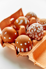 Picture of chicken eggs painted with various white patterns in colorful orange cardboard container. Easter concept