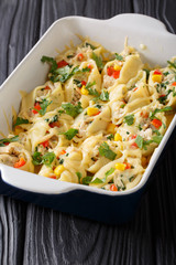 Baked pasta conchiglioni with cheese, chicken, mushrooms and vegetables close-up in a baking dish. vertical