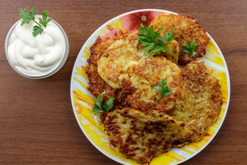 Homemade fried potato pancakes with sour cream on wooden table