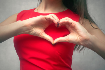 Love heart. Girl is holding hands in the shape of heart on a background of red dress.