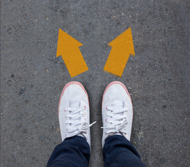 Pair of shoes standing on a tarmac road with two arrows