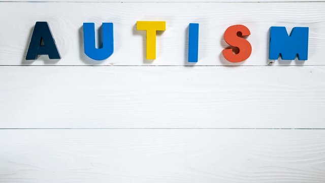 Word AUTISM and hand with a piece of puzzle on white wooden background, top view. Autism Spectrum Disorder (ASD). Autism awareness. Word Autism gathering from letters, stop motion, animation.
