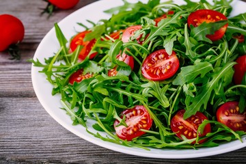 fresh green salad with arugula and red tomatoes on wooden background
