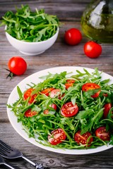 fresh green salad with arugula and red tomatoes on wooden background