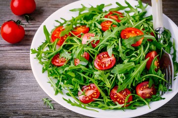 fresh green salad with arugula and red tomatoes on wooden background