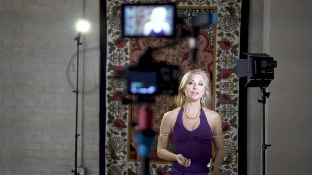Wide settling shot of mature woman vlogger talking to camera on a well lit set.