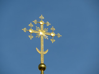 Golden Christian cross shining on blue sky background. Easter concept