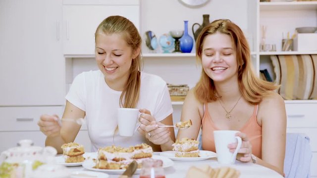 Girlfriends are watching TV and drfinking tea at home.