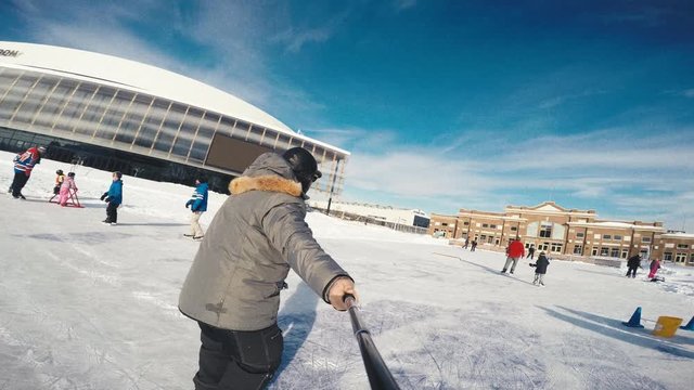 A happy man film himself ice-skating in a beautiful winter day in front of Quebec city's  Hockey stadium.